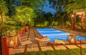 a backyard pool with chairs and a table next to a table at Hostie Tranquil Greens farmhouse near Golf course road Gurgaon in Gurgaon