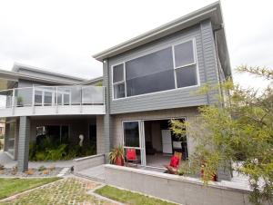 a house with a balcony and red chairs in the yard at Bay Breeze Accommodation in Cooks Beach