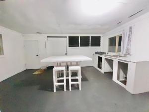 a white kitchen with a table and two stools at Private Double Room - Airport Cottage in Fua‘amotu
