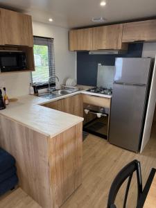 a kitchen with wooden cabinets and a stainless steel refrigerator at Mobilhome Cap'Oceha SIBLU-Les Viviers 4étoiles in Lège-Cap-Ferret