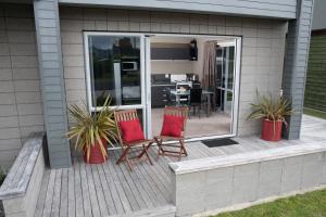 ein Haus mit 2 Stühlen und einer Terrasse mit einem Tisch in der Unterkunft Bay Breeze Accommodation in Cooks Beach