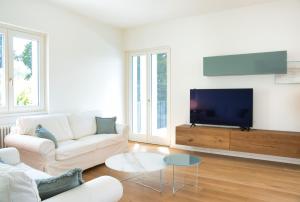 a white living room with a white couch and a tv at Hidden Gem - Villa with private swimmingpool Bellagio view in Lierna