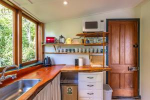 a kitchen with a sink and a counter with a microwave at Splashing Tūi Cottage in Waiheke Island +8 photos