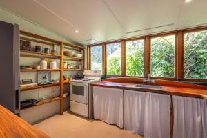 a kitchen with a counter and a sink and some windows at Splashing Tūi Cottage in Waiheke Island