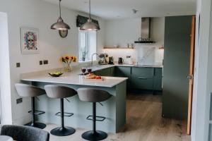 a kitchen with green cabinets and a counter with stools at A Spacious Countryside Retreat for up to 16 Guests in Llanarthney