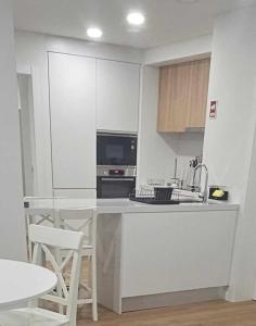 ポンタ・デルガダにあるApartamento Sonho Brisaの白いキャビネットとテーブルと椅子のあるキッチン