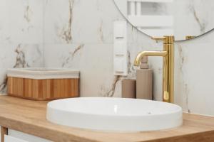 La salle de bains est pourvue d'un lavabo blanc et d'un robinet en or. dans l'établissement Apartament Komfort, à Uniejów 4 autres photos