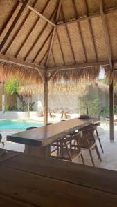 a picnic table under a straw umbrella next to a pool at Sayamaya - Soft Opening in Gili Islands