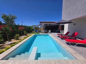 a swimming pool with red chairs and an umbrella at villa Amethyst in Lozenets