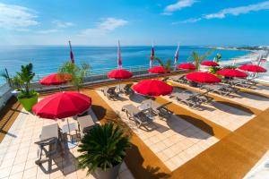 um pátio exterior com guarda-sóis e cadeiras vermelhas e o oceano em Aparthotel Adagio Nice Promenade des Anglais em Nice