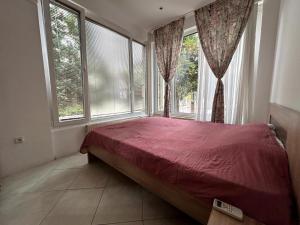 a bedroom with a bed and two large windows at Peaceful apartment with yard and parking in Skopje