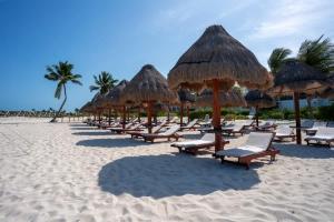 a row of straw umbrellas and chairs on a beach at 3BR Beachfront Luxury Apt w/First Class Amenities in Cancún +54 photos