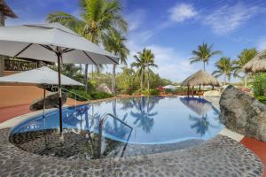a swimming pool with an umbrella and palm trees at Hilton Grand Vacations Club Zihuatanejo in Zihuatanejo