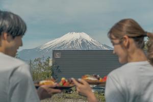 two people holding plates of food with a mountain in the background at GLANSTELLA CABIN Fujiyamanakako in Yamanakako