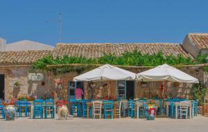 a group of tables and chairs with white umbrellas at 2 Bedroom Beautiful Apartment In Marzamemi in Marzamemi +27 photos