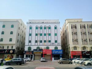ein großes weißes Gebäude mit auf einem Parkplatz geparkten Autos in der Unterkunft Cozy Vibes Hostel in Muscat