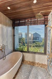 une baignoire dans une salle de bain avec une grande fenêtre dans l'établissement Biệt Thự Hội An View, à Thanh Ðông (1)