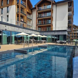 a swimming pool in front of a building with tables and umbrellas at Happy Valley Resort Szklarska Poręba in Szklarska Poręba