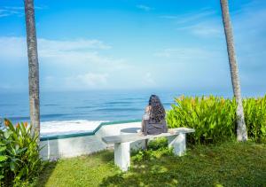 a woman sitting on a bench looking at the ocean at Solaris Beach View Resort & Spa by VOYE HOMES in Varkala