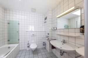 a white tiled bathroom with a sink and a toilet at Hotel Casa Nostra in Schloß Holte-Stukenbrock
