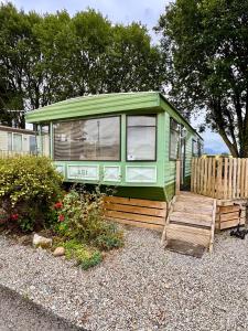 a green house with a wooden porch and a fence at No 26 Mountain View in Cockermouth