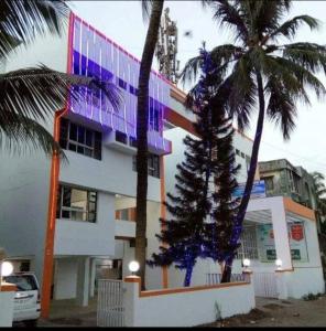a building with a palm tree in front of it at Hotel Guruji in Alibag