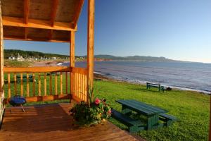 een houten veranda met een picknicktafel en een bank op het strand bij Chalets Nature Océan in Perce