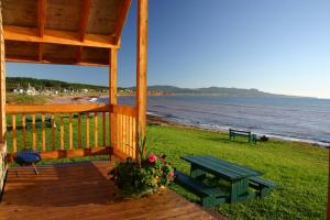 a wooden porch with a picnic table and a bench on the beach at Chalets Nature Océan in Perce