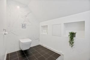 a white bathroom with a toilet and a tile floor at Top-Floor Gem with City Views in Bergen