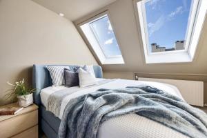a bedroom with a bed with a blanket and two windows at Top-Floor Gem with City Views in Bergen