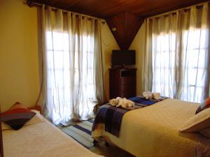 a bedroom with two beds and a tv and windows at Pousada Refúgio Akatu in Campos do Jordão +7 photos