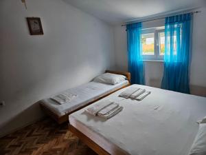 two beds in a room with blue curtains and a window at Apartmani Štefica in Dramalj