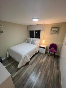 ein Schlafzimmer mit einem weißen Bett und einem lila Stuhl in der Unterkunft Departamento céntrico en Huaraz in Huaraz