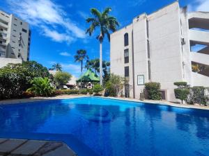 a swimming pool in front of a building with a palm tree at Tus vacaciones Ideales en Costa Azul Isla de Margarita in Porlamar