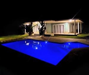 a blue swimming pool in front of a house at night at Quarto-Suíte Serra Petrópolis in Petrópolis