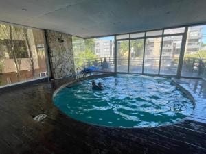 two people swimming in a large pool in a building at Depto 24 Punta Pampa in Las Gaviotas