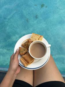 a person holding a plate of food and a cup of coffee at Nirvan Stays with Pool ,Indore Bhopal Highway 