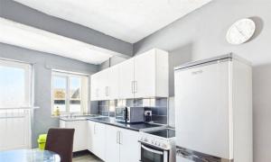 a kitchen with white cabinets and a clock on the wall at Rhyl Aparthotels in Rhyl