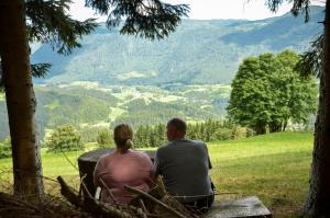 a man and woman sitting on a bench looking at a valley at Koča v Lozah in Gornji Grad