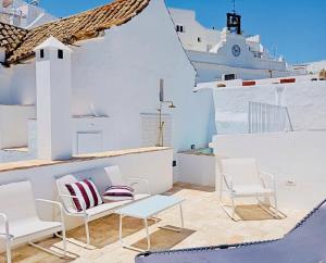 a balcony with white chairs and a bench and a ship at Plaza España 5 Casa con encanto, terraza y vistas in Vejer de la Frontera