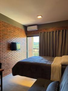 a bedroom with a bed and a tv on a brick wall at Villa da Serra Studios Ibitipoca in Conceição da Ibitipoca