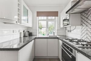a white kitchen with a stove and a window at Bright 2bed flat near station - COU A in Coulsdon