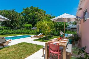 einen Tisch mit Stühlen und einen Sonnenschirm neben einem Pool in der Unterkunft The Coral Cabana Modern Palm Beach Escape in West Palm Beach