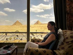 Una mujer sentada en un sofá mirando por una ventana las pirámides. en Nader home, en Giza