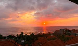 - un coucher de soleil sur l'océan avec des maisons et des bâtiments dans l'établissement Pooja Ocean View Cottage, à Nusa Penida