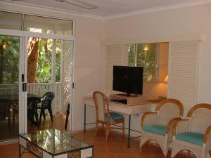 a living room with a desk with a television and chairs at Palm Cove Tropic Apartments in Palm Cove