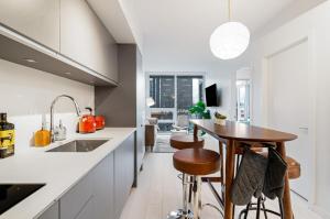 a kitchen with white counters and a wooden table at Modern 4-Bed Condo with AC and Parking near SkyTrain for 6 in Vancouver +38 photos