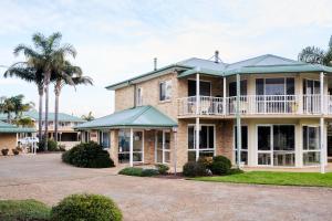 a large brick house with a balcony and palm trees at Harbourview House Apartment in Bermagui
