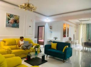 班加罗尔Room in a 3bhk的一位女士坐在客厅的黄色沙发上，手里拿着一台笔记本电脑 更多1张照片