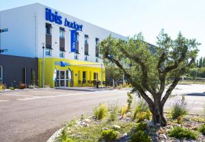 a building with a tree in front of it at Ibis Budget Porte de Camargue in Saint-Martin-de-Crau